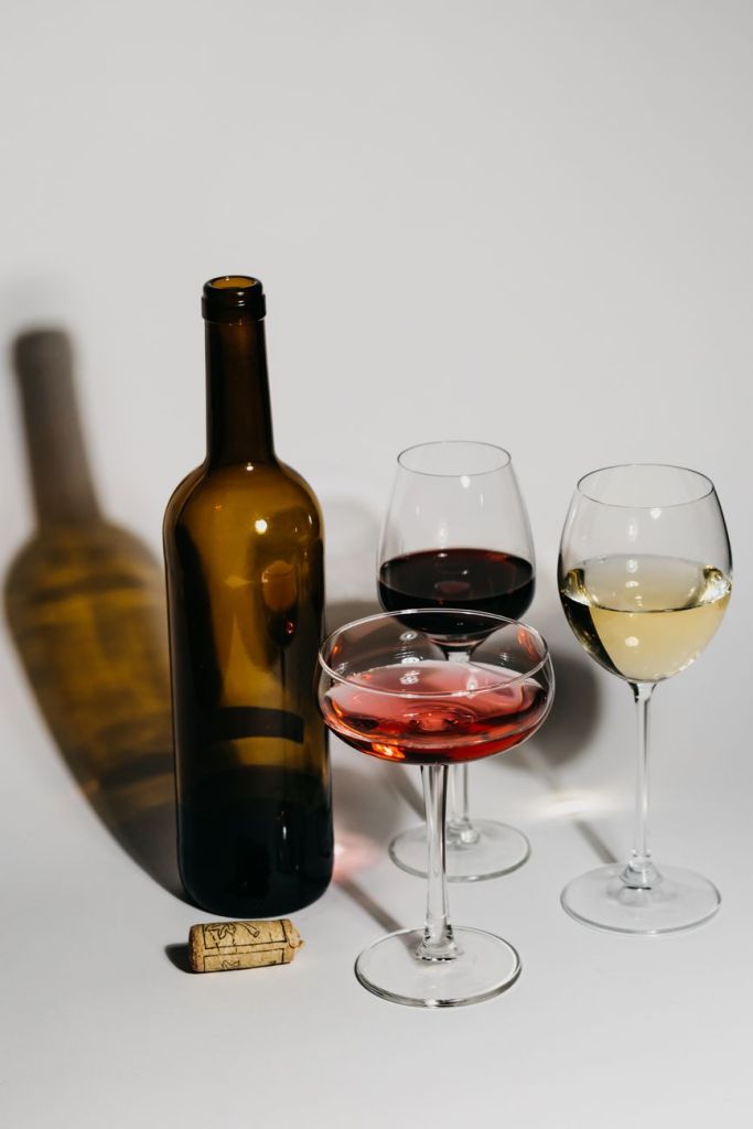 A wine bottle beside glasses of red, rosé and white wine on a white table